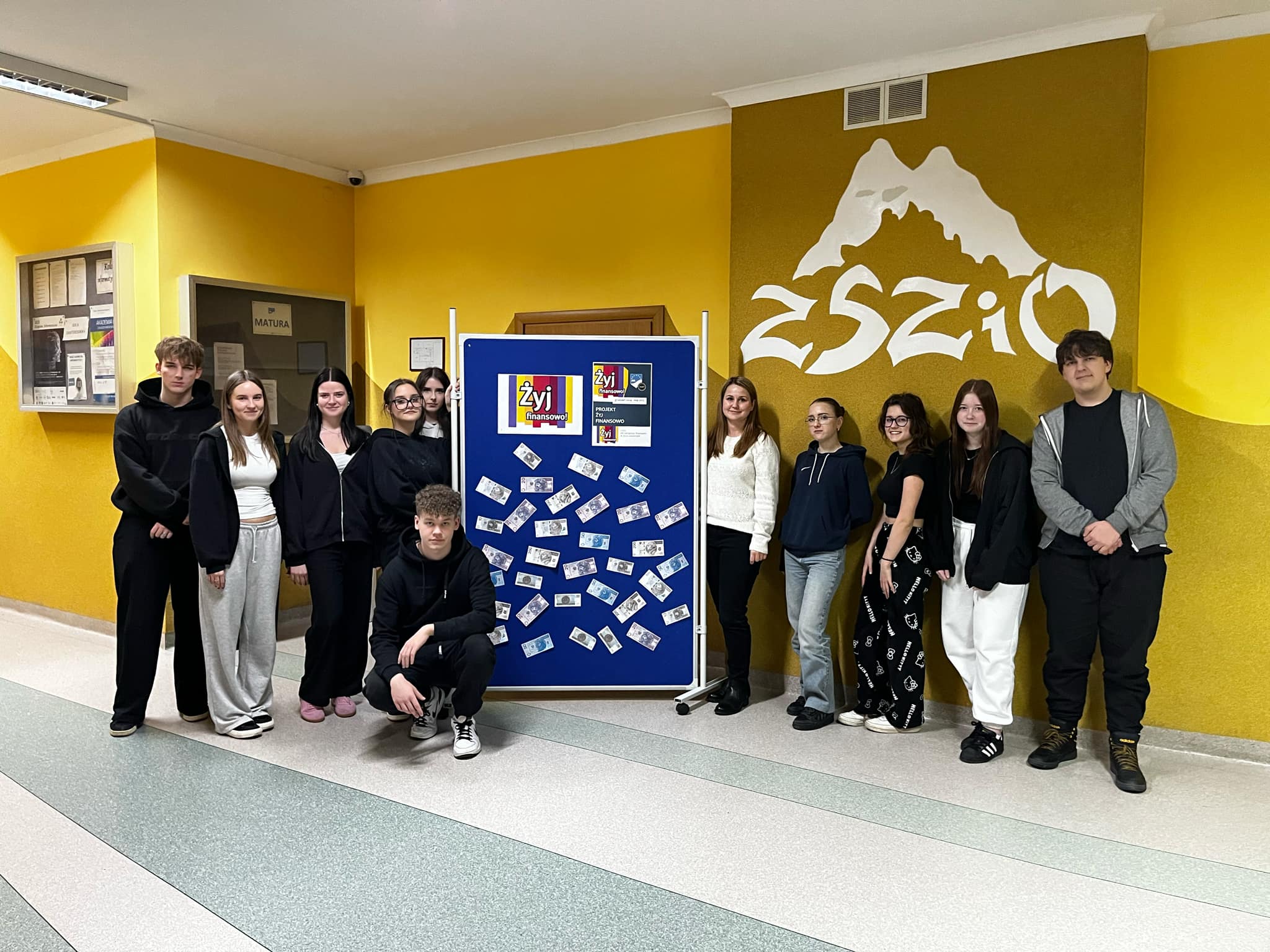 Pani Maria Dymek wraz uczestnikami projektu stoją przed tablicą poświęconą projektowi. Pani Maria Dymek wraz uczestnikami projektu stoją przed tablicą poświęconą projektowi.